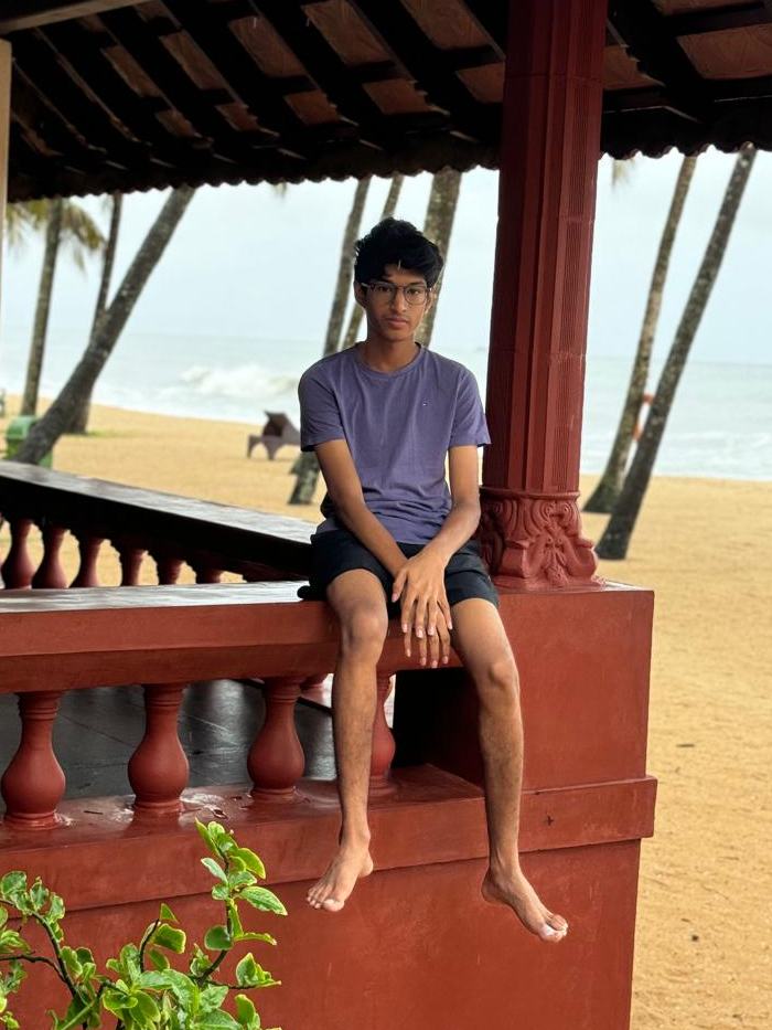 Vihaan Shetty sitting on a red balustrade at a beach pavilion